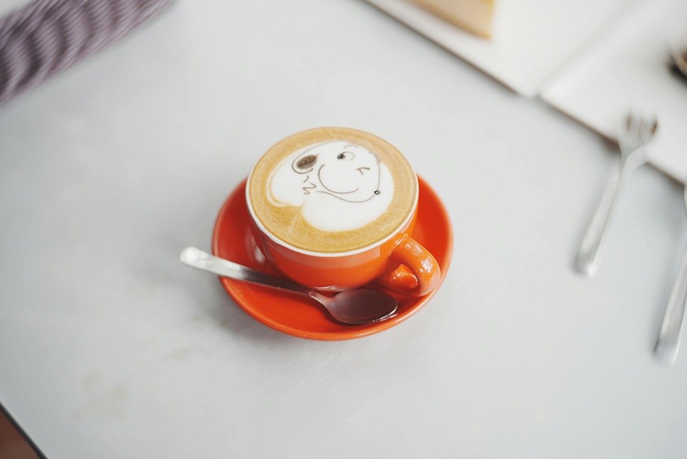 Latte art in an orange mug, winking face